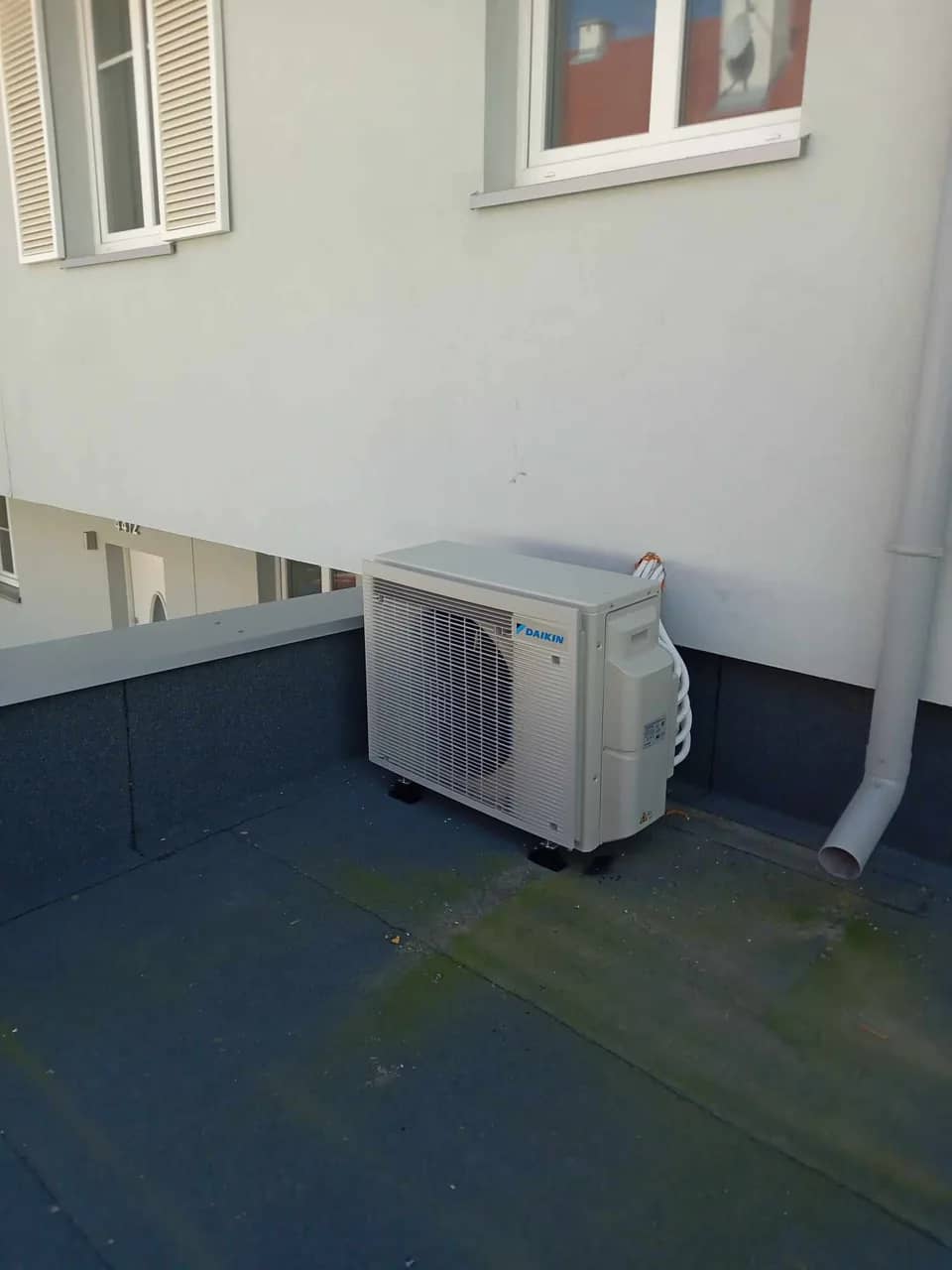 Jednostka zewnętrzna klimatyzacji Daikin ustawiona na dachu płaskim pokrytym niebieską membraną