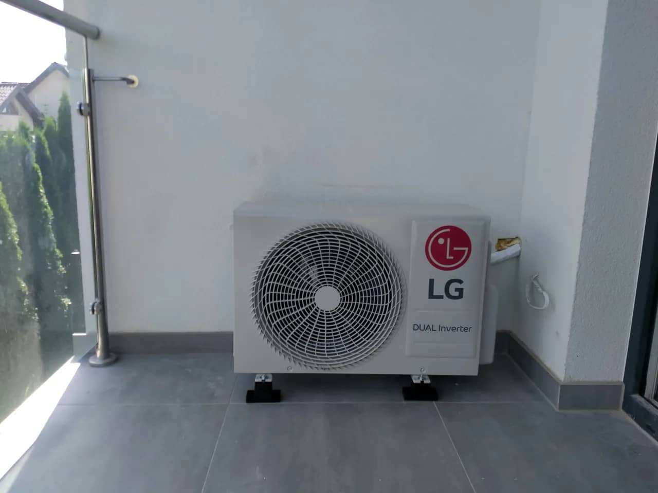 Jednostka zewnętrzna LG Dual Inverter na tarasie przy tujach i metalowej barierce