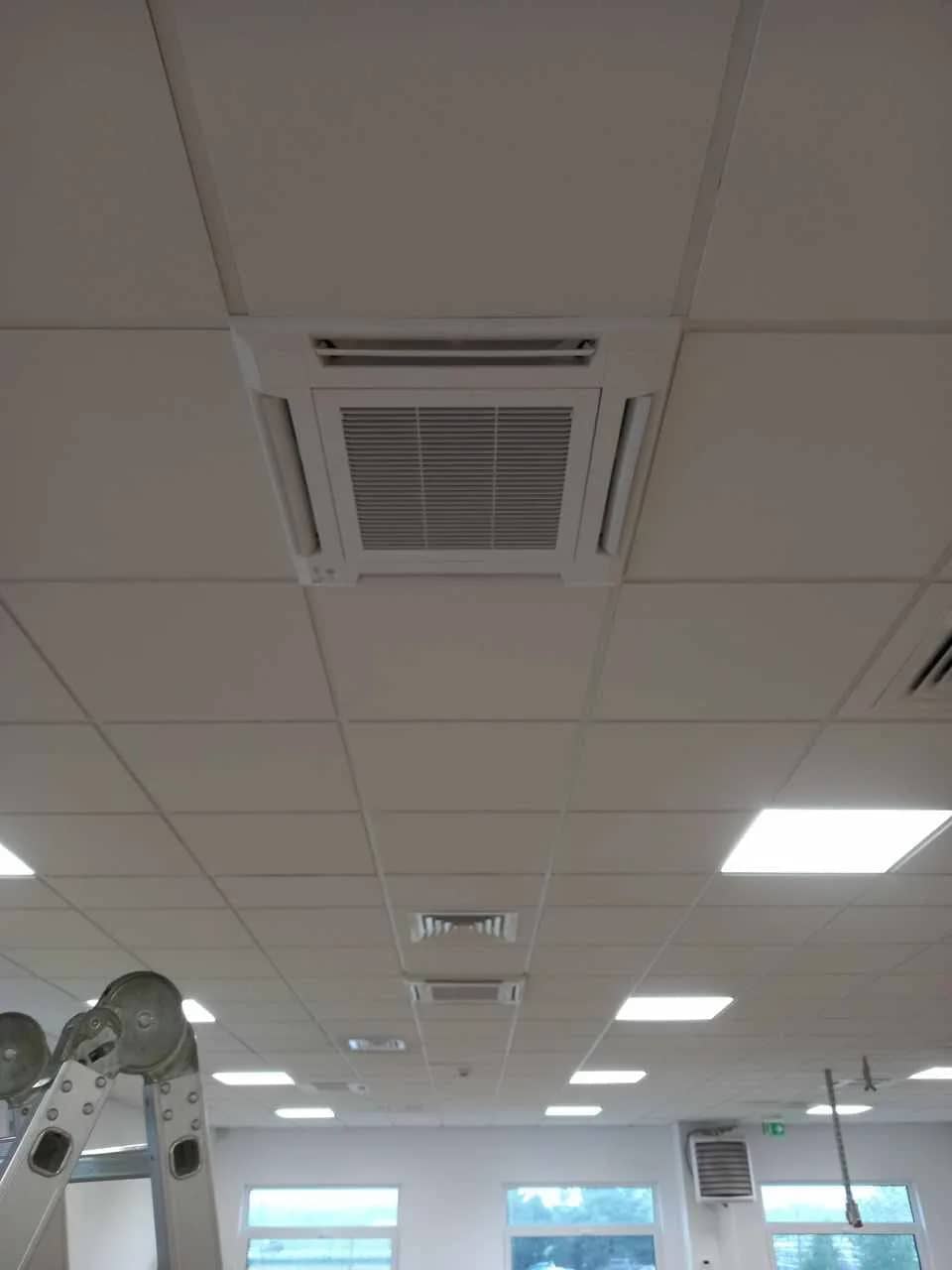Otwarta przestrzeń biurowa z sufitem podwieszanym, oprawami LED i wpuszczoną kasetą klimatyzacji