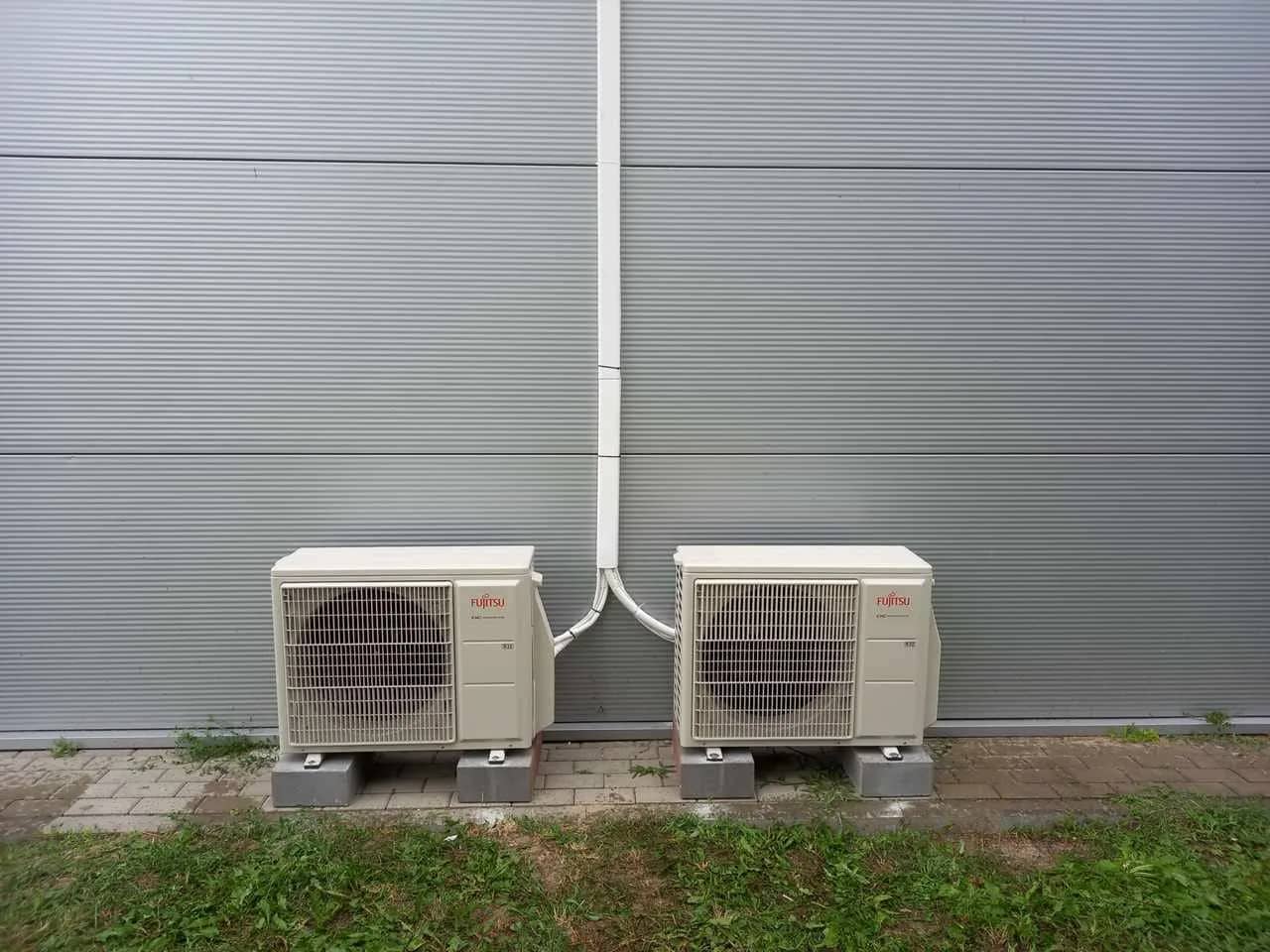 Dwie jednostki zewnętrzne klimatyzacji ustawione na podestach przy szarej elewacji hali z płyty warstwowej