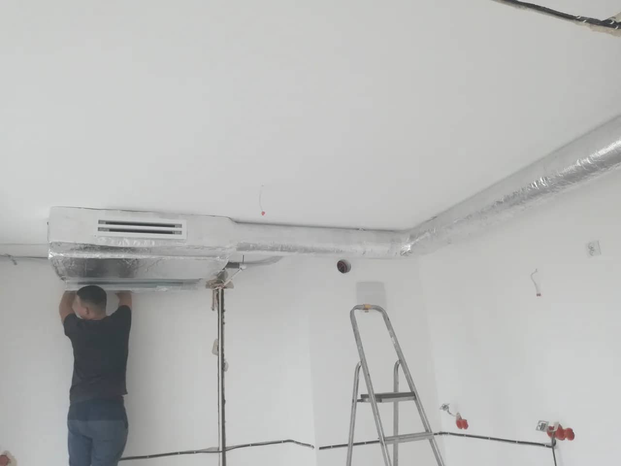 Monter mocujący jednostkę kanałową klimatyzacji pod sufitem pomieszczenia w trakcie wykończenia