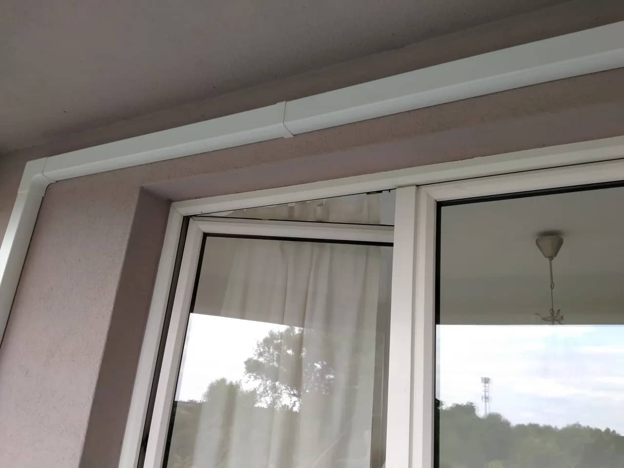 Biała listwa maskująca instalację klimatyzacji poprowadzona przy suficie i drzwiach balkonowych