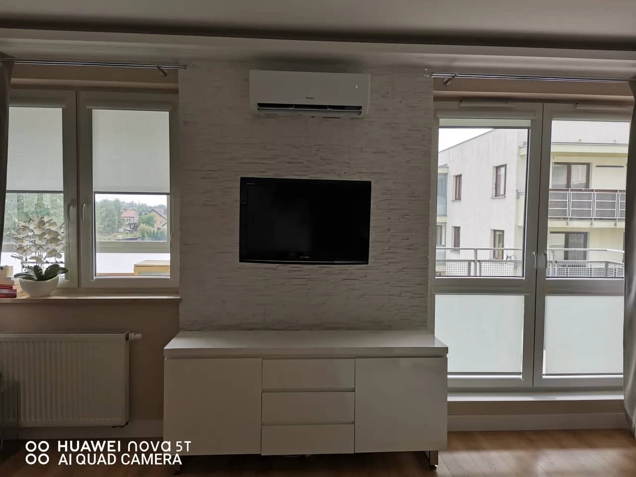 Klimatyzator ścienny zamontowany nad ścianą telewizyjną wykończoną jasnym kamieniem dekoracyjnym