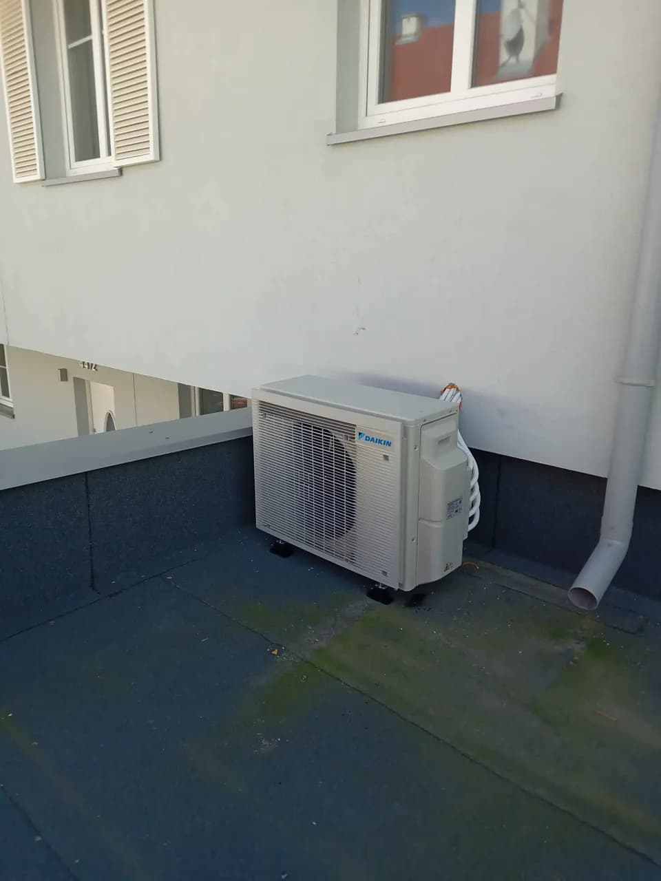 Jednostka zewnętrzna klimatyzacji Daikin ustawiona na dachu płaskim pokrytym niebieską membraną