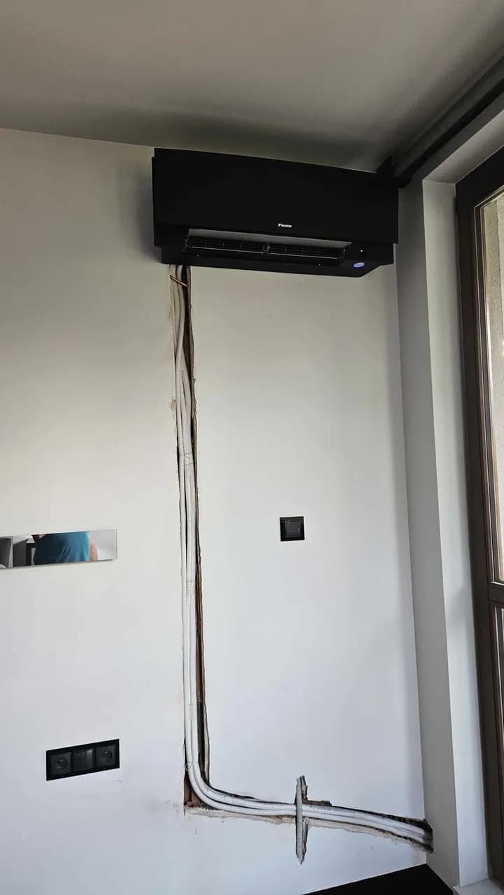 Ciemny klimatyzator ścienny w pokoju z bruzdą prowadzącą w dół ściany