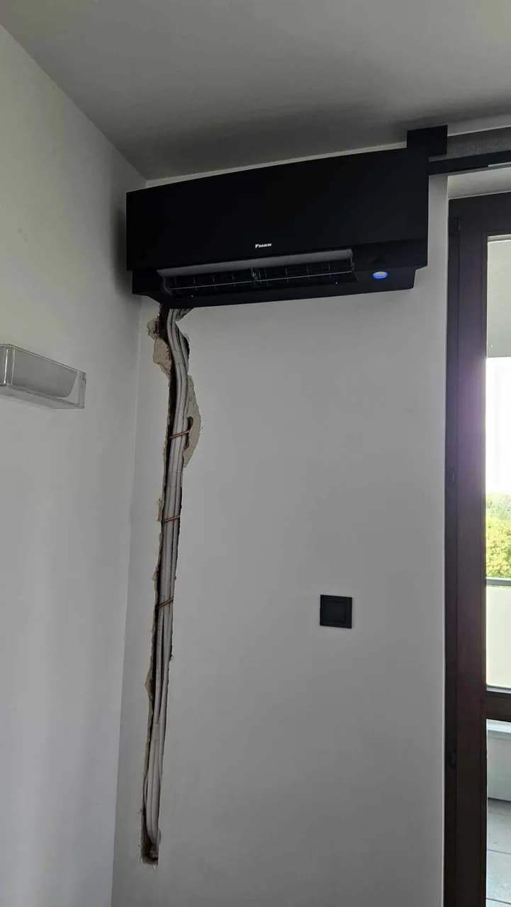 Klimatyzator ścienny przy przeszkleniu, poniżej bruzda z ułożoną instalacją