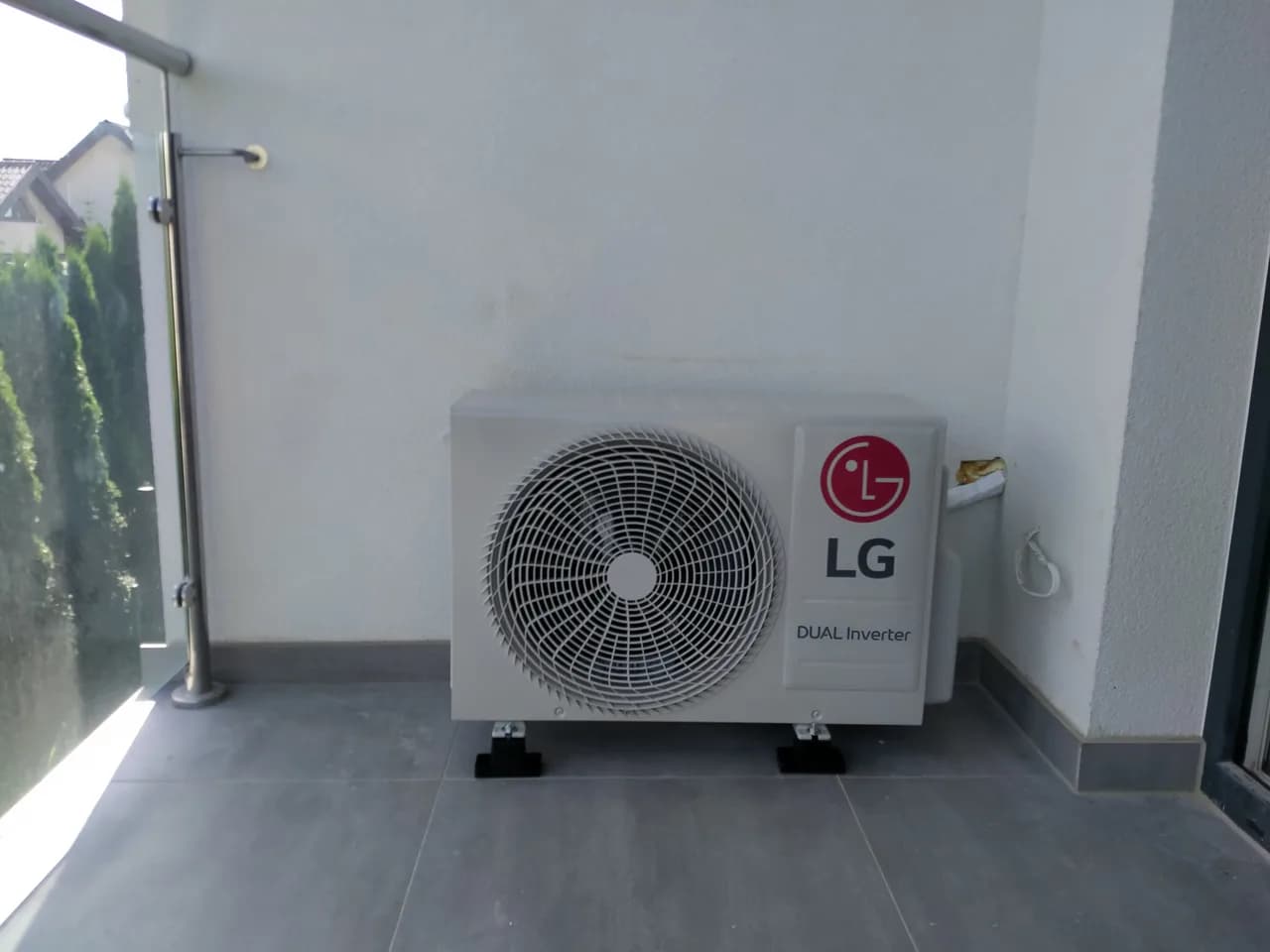 Jednostka zewnętrzna LG Dual Inverter na tarasie przy tujach i metalowej barierce