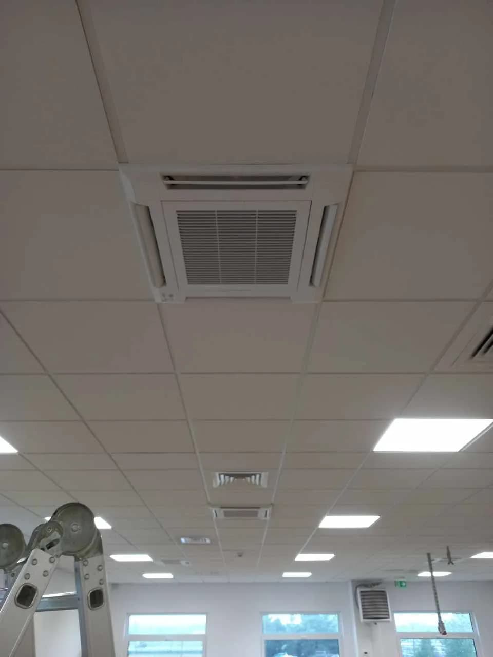 Otwarta przestrzeń biurowa z sufitem podwieszanym, oprawami LED i wpuszczoną kasetą klimatyzacji