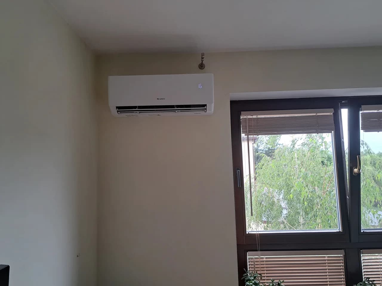 Klimatyzator ścienny w wykończonym pokoju z drewnianym oknem i widokiem na łąkę