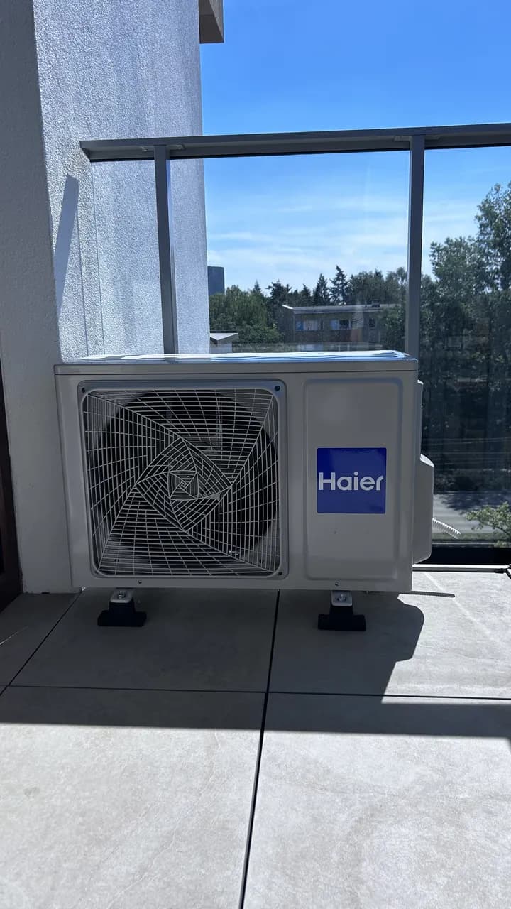 Jednostka zewnętrzna Haier ustawiona nad płytkami obok szklanej balustrady