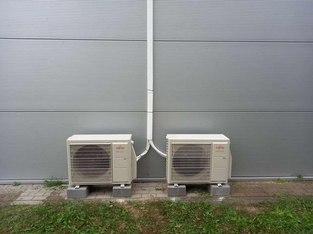 Dwie jednostki zewnętrzne klimatyzacji ustawione na podestach przy szarej elewacji hali z płyty warstwowej