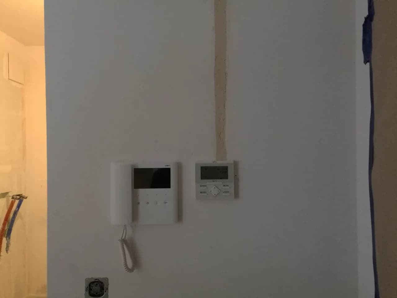 Panel sterownika przewodowego klimatyzacji na ścianie obok wideodomofonu