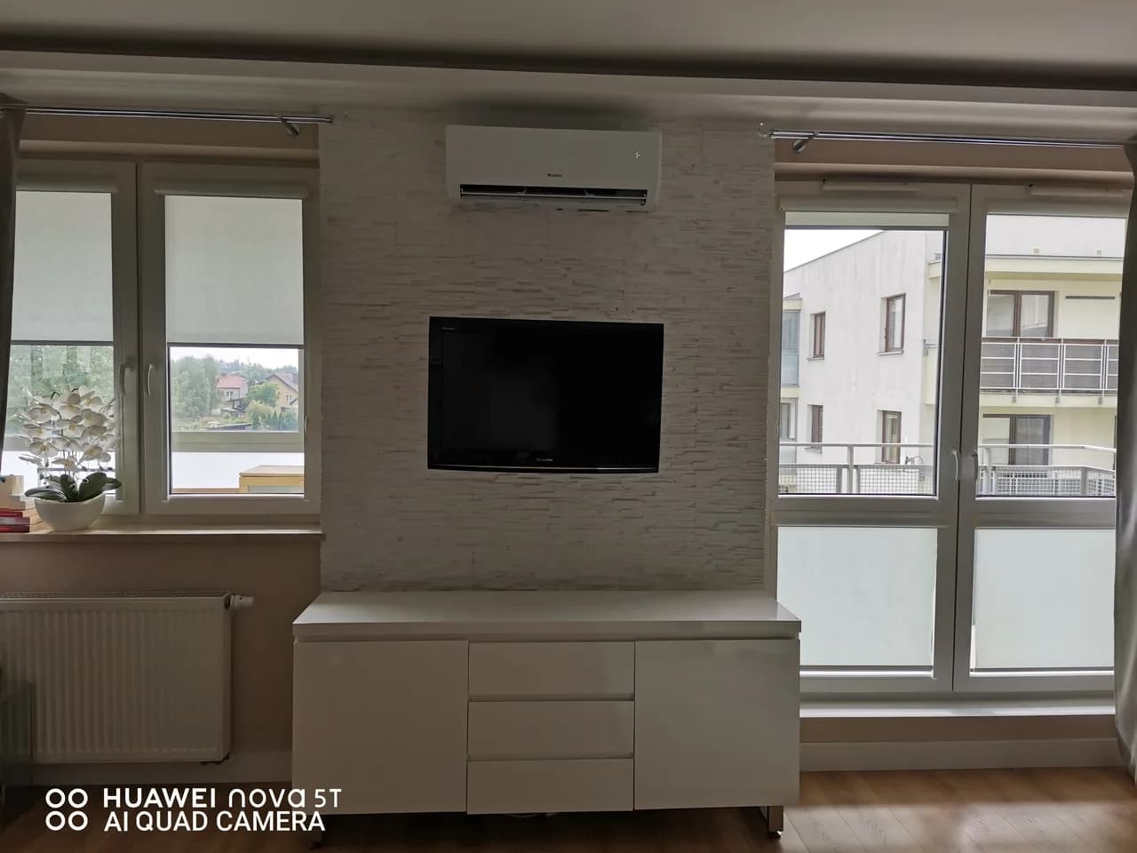 Klimatyzator ścienny zamontowany nad ścianą telewizyjną wykończoną jasnym kamieniem dekoracyjnym