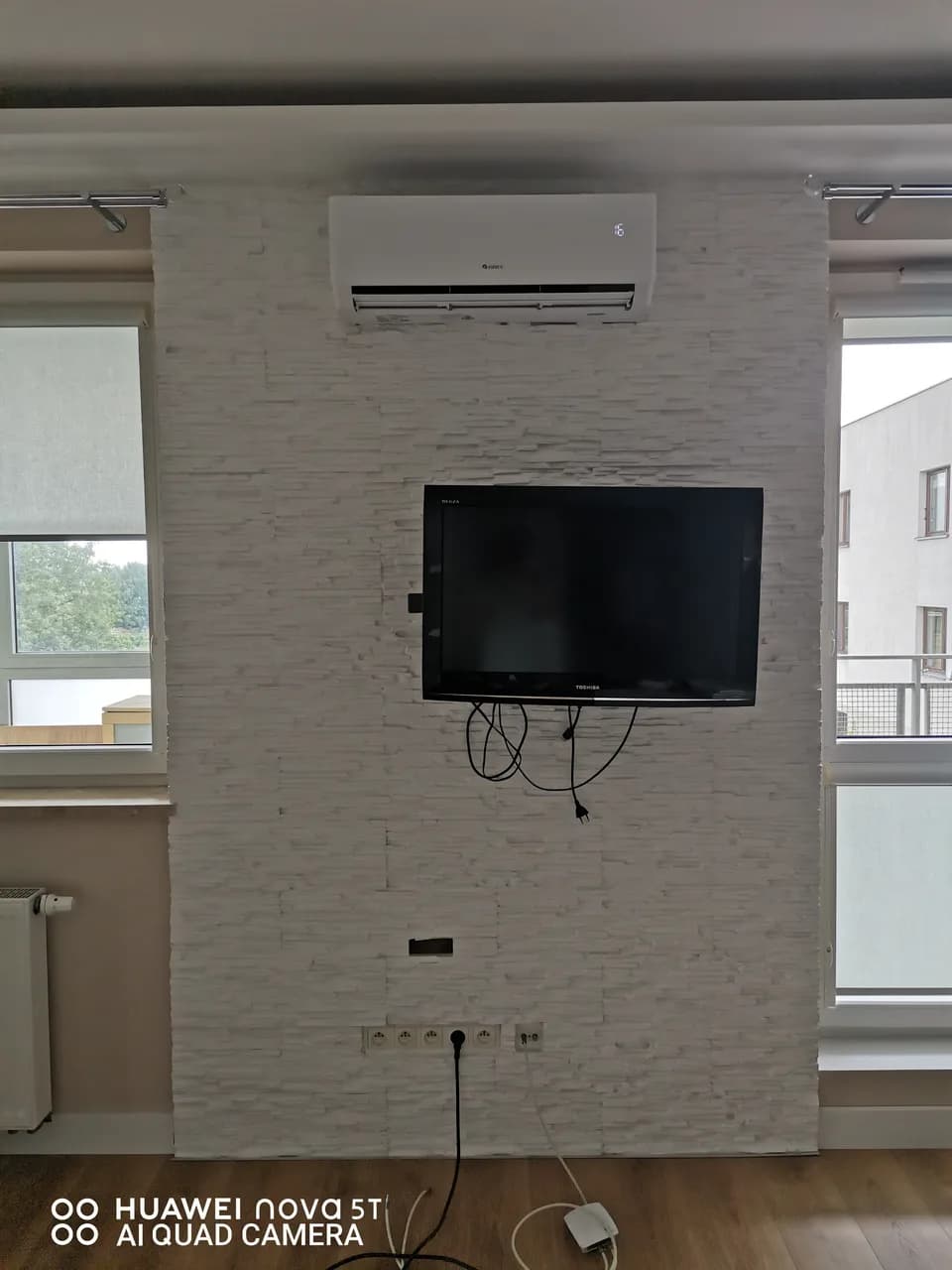 Ściana z kamienną okładziną i telewizorem, nad nią klimatyzator, kable jeszcze nieschowane