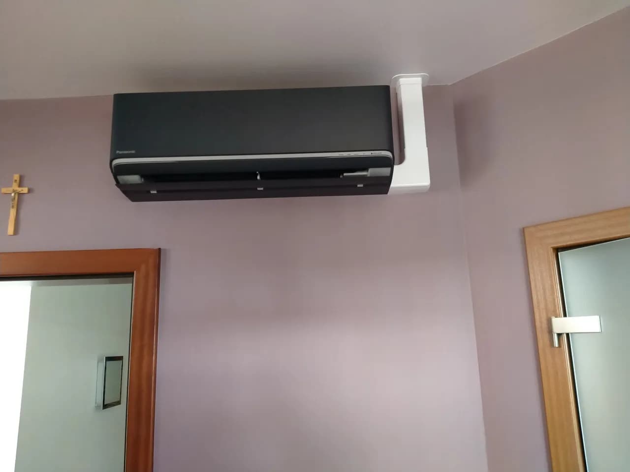 Grafitowy klimatyzator ścienny na jasnoróżowej ścianie pokoju na poddaszu