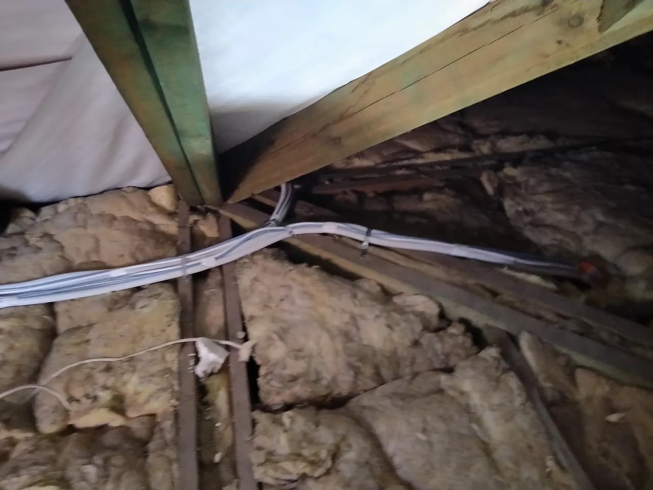 Instalacja chłodnicza w białej izolacji przechodząca przez wełnę mineralną między drewnianymi jętkami dachu