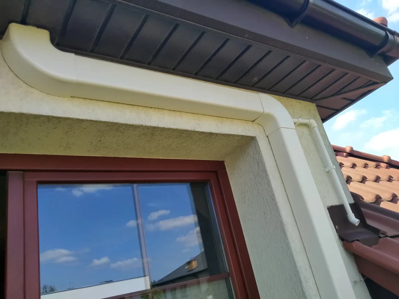 Biała listwa maskująca instalację klimatyzacji poprowadzona pod okapem dachu nad oknem