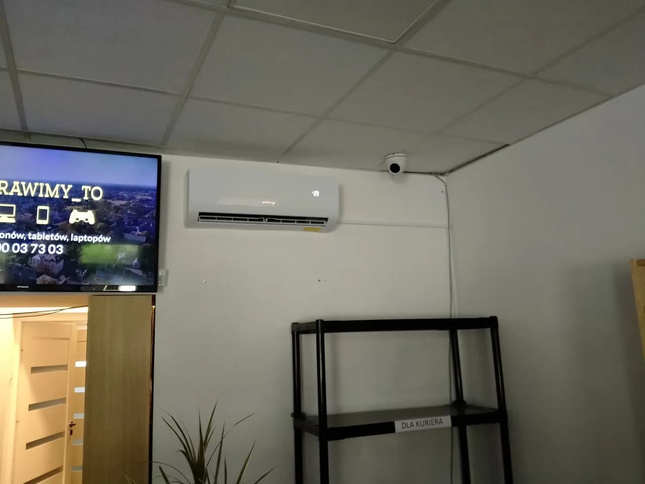 Klimatyzator ścienny w części lokalu dla klientów, obok telewizor z reklamą serwisu