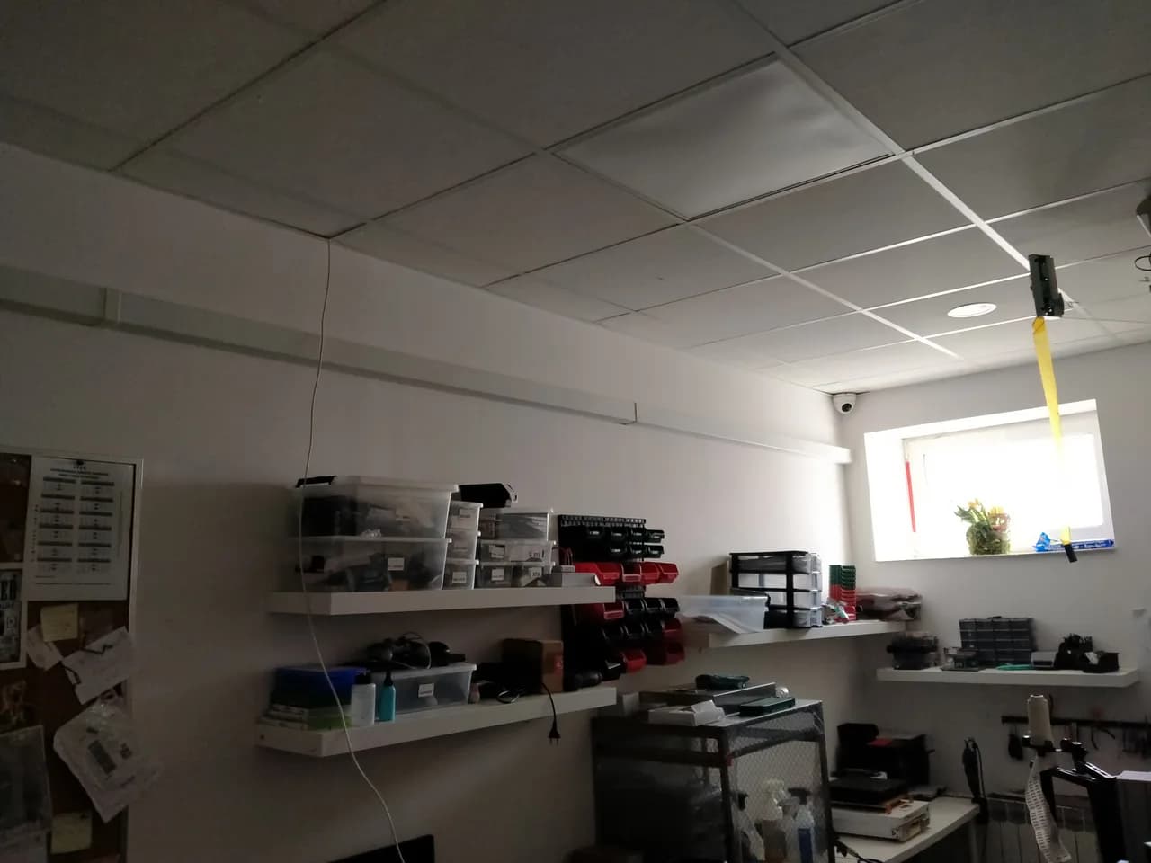 Biała listwa instalacyjna prowadzona pod sufitem podwieszanym nad regałami z częściami