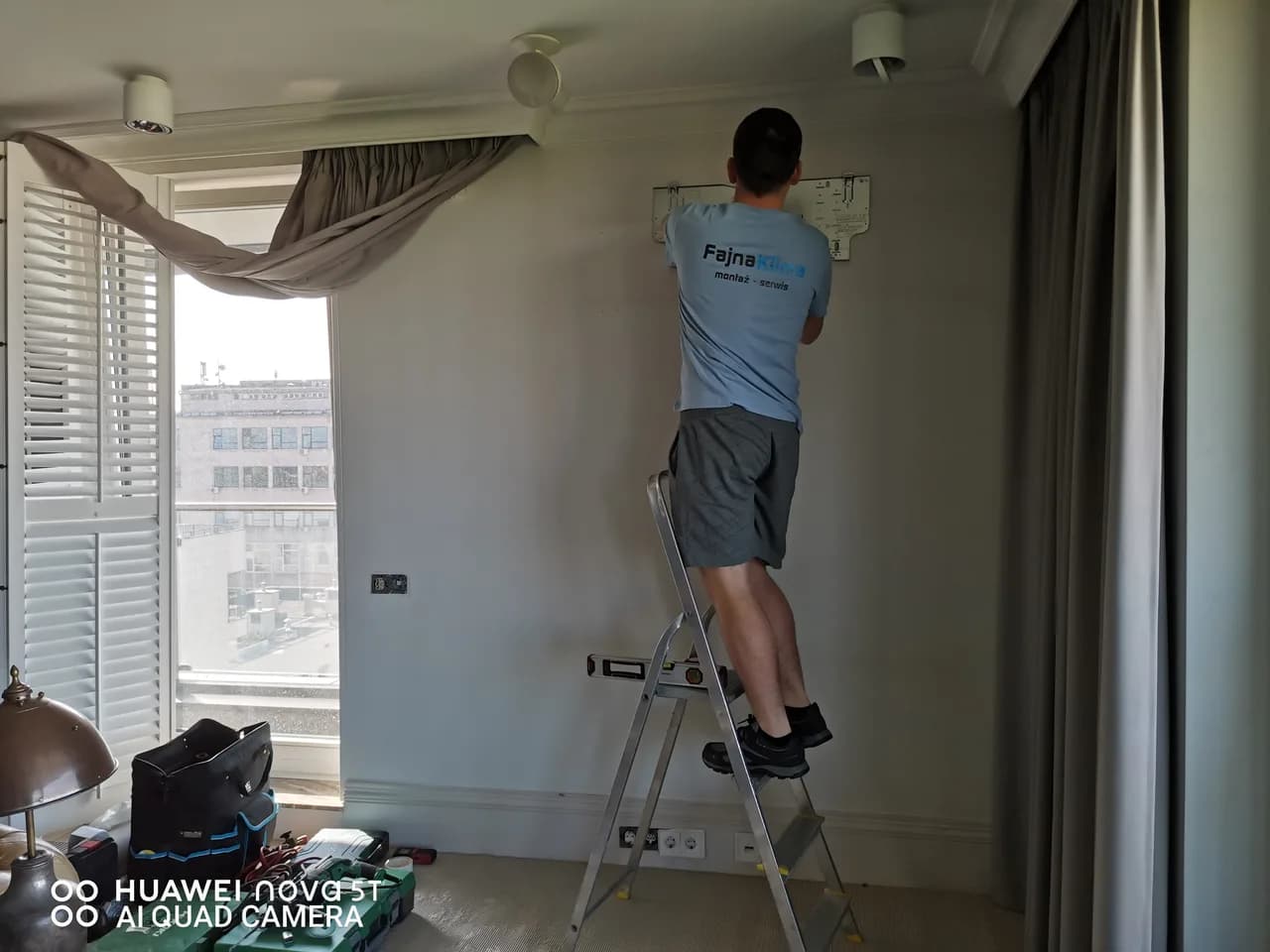 Monter na drabinie przy oknie apartamentu z widokiem na dachy miasta