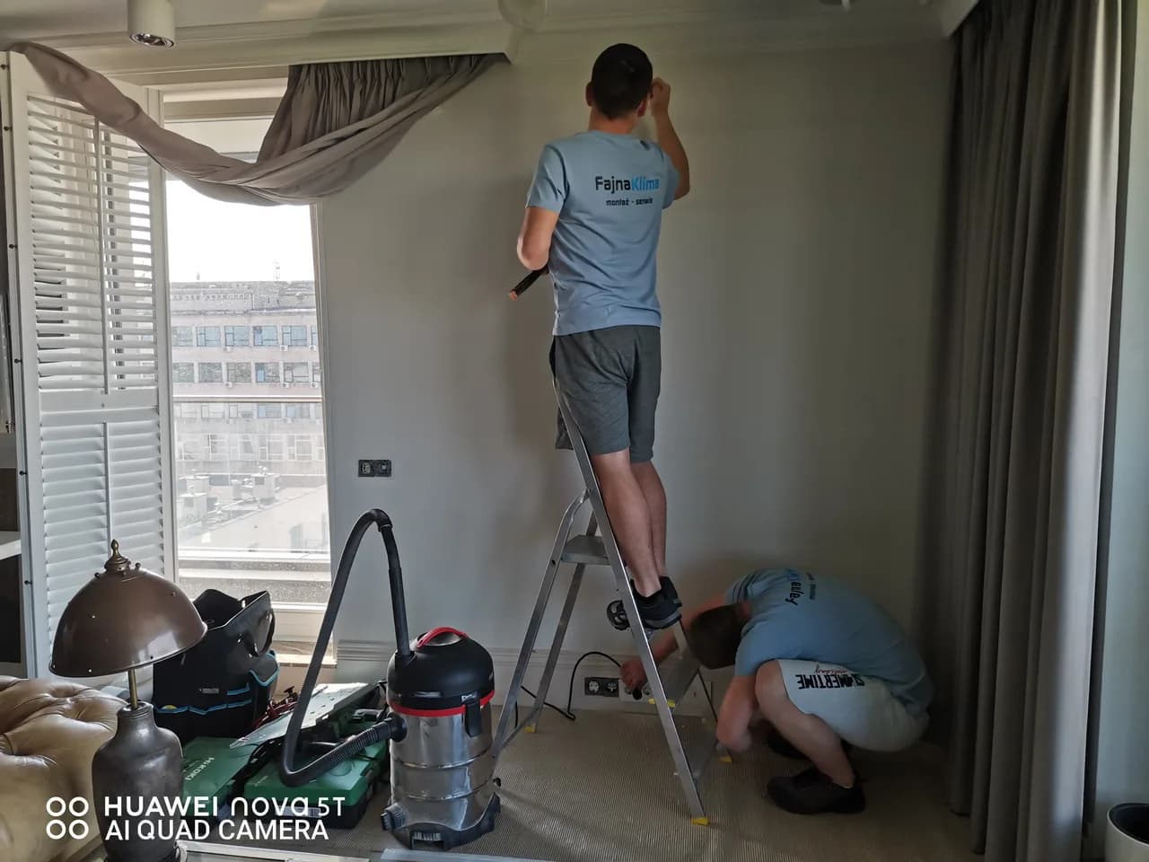 Dwóch monterów przy pracy, odkurzacz przemysłowy i drabina w umeblowanym apartamencie