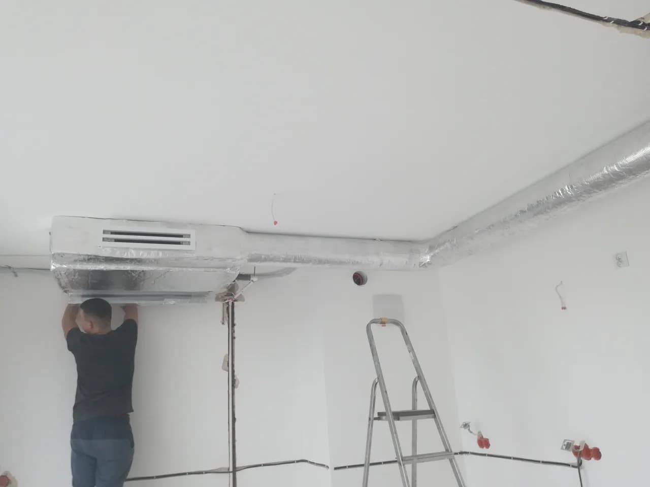 Monter mocujący jednostkę kanałową klimatyzacji pod sufitem pomieszczenia w trakcie wykończenia