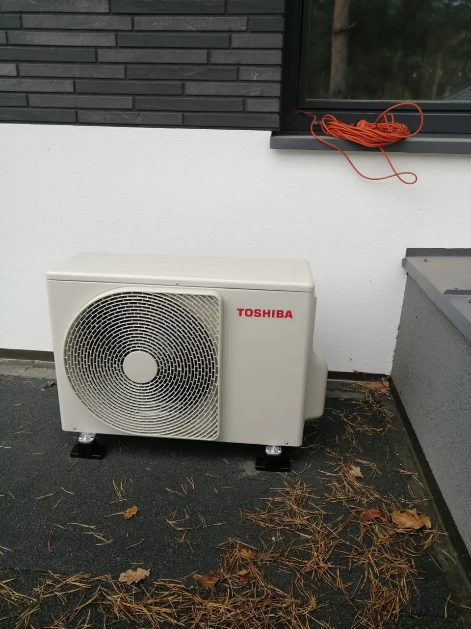 Zbliżenie jednostki Toshiba i czarnych stóp na dachu z papą, igliwiem i liśćmi