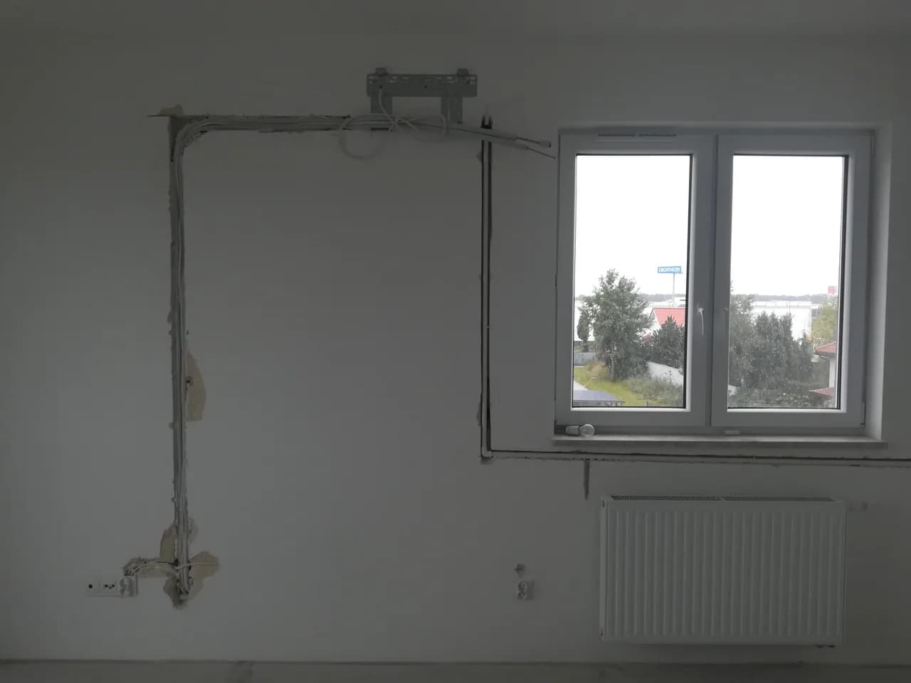 Bruzda z instalacją i płyta montażowa klimatyzatora na nieotynkowanej ścianie przy oknie