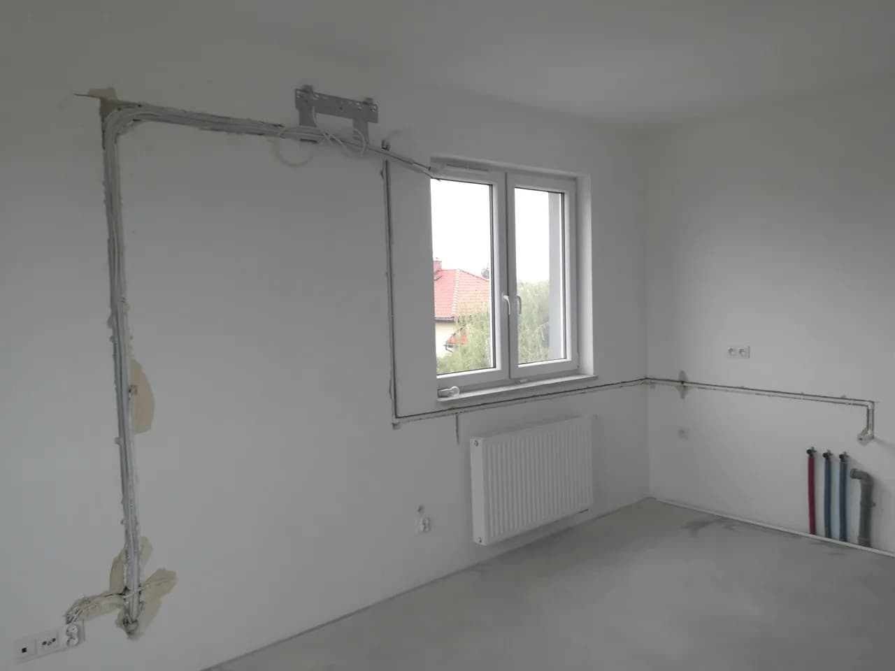 Pokój w domu w budowie z surowymi ścianami, grzejnikiem pod oknem i przygotowaną instalacją