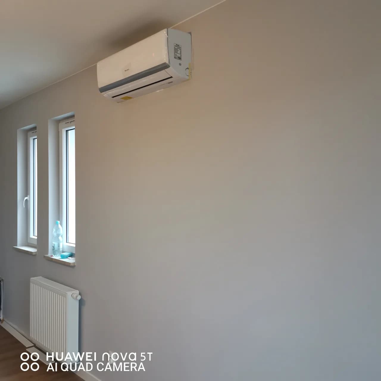 Klimatyzator ścienny nad grzejnikiem w pokoju z dwoma wąskimi oknami