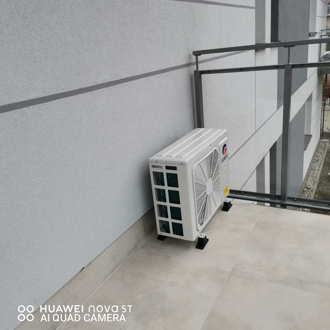 Loggia z jednostką zewnętrzną klimatyzacji przy ścianie i szklaną balustradą