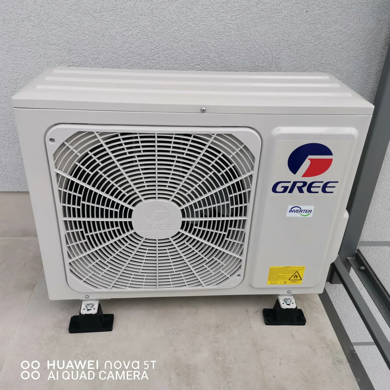 Jednostka zewnętrzna GREE Inverter stojąca na płytkach loggii przy jasnej ścianie